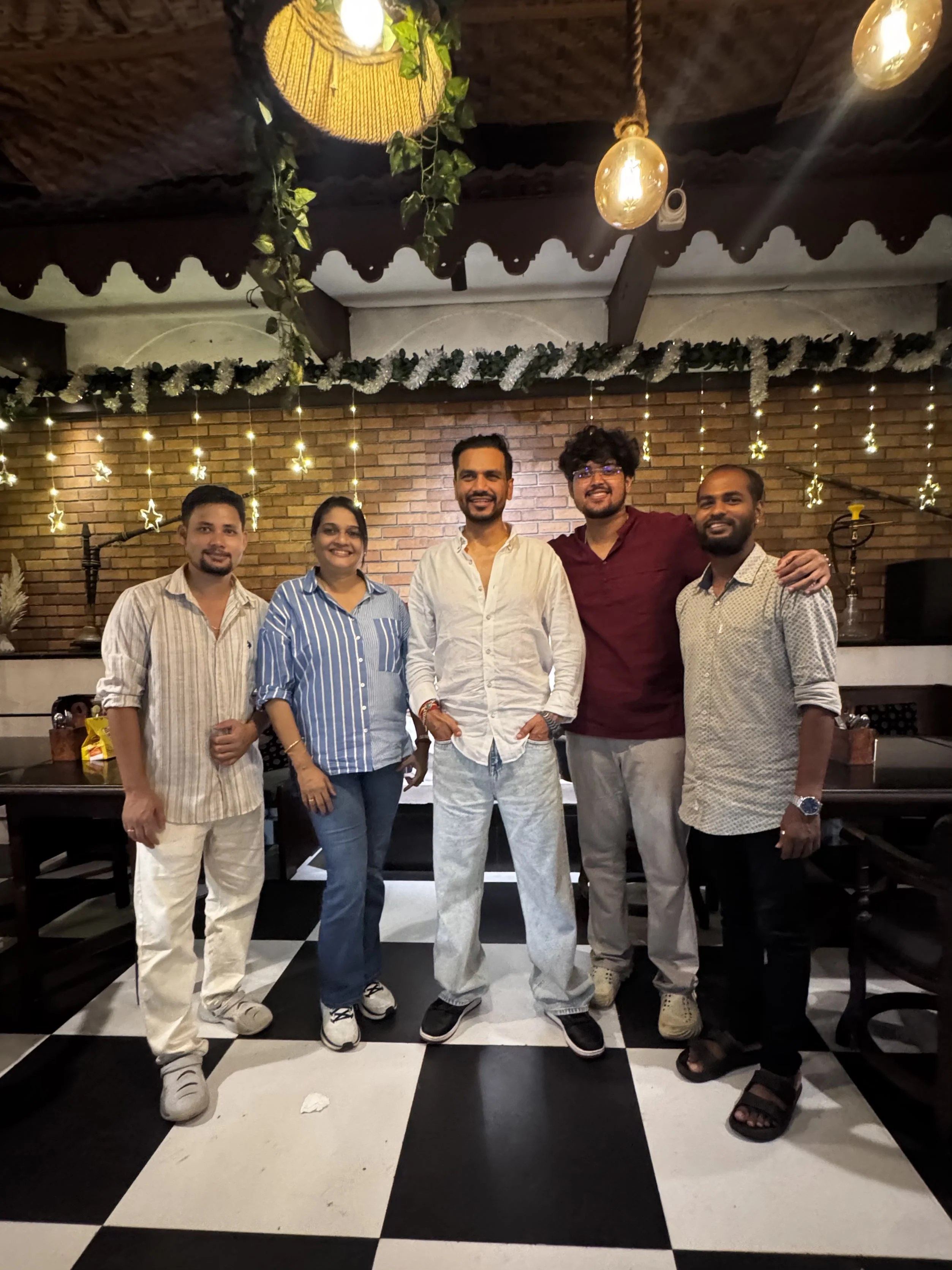 Five guests together on the chequered floor under the string lights